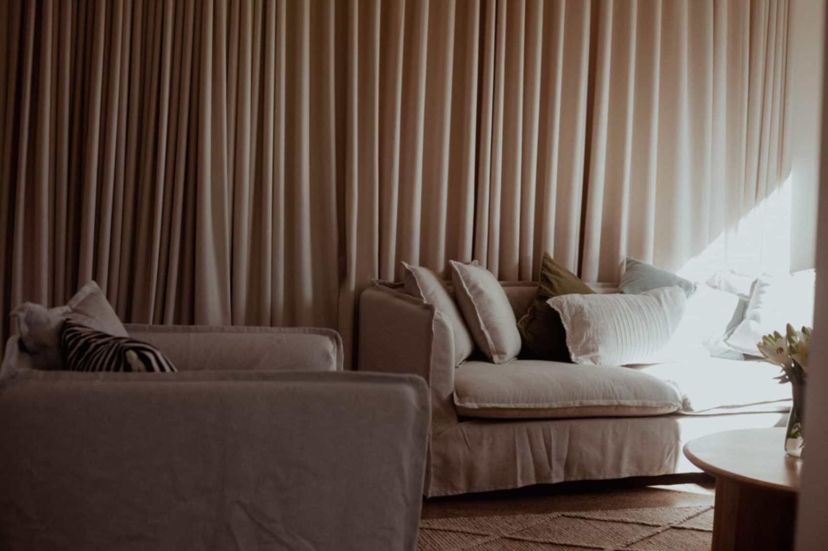 Living room with couch, pillows, and curtains, with circular table in middle with vase of flowers