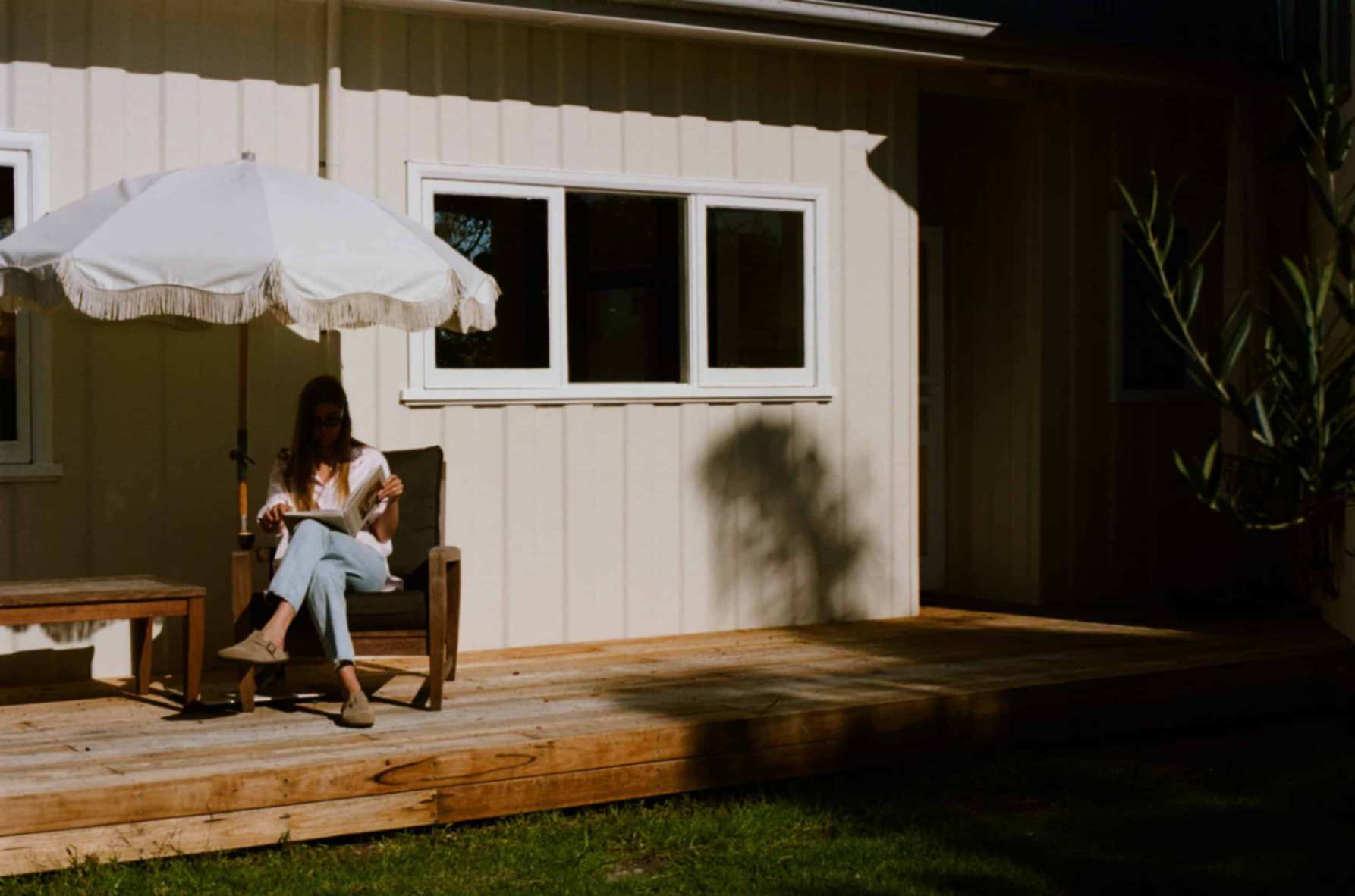 Person sitting and reading on outdoor chair outside of Merimbula holiday rental under umbrella