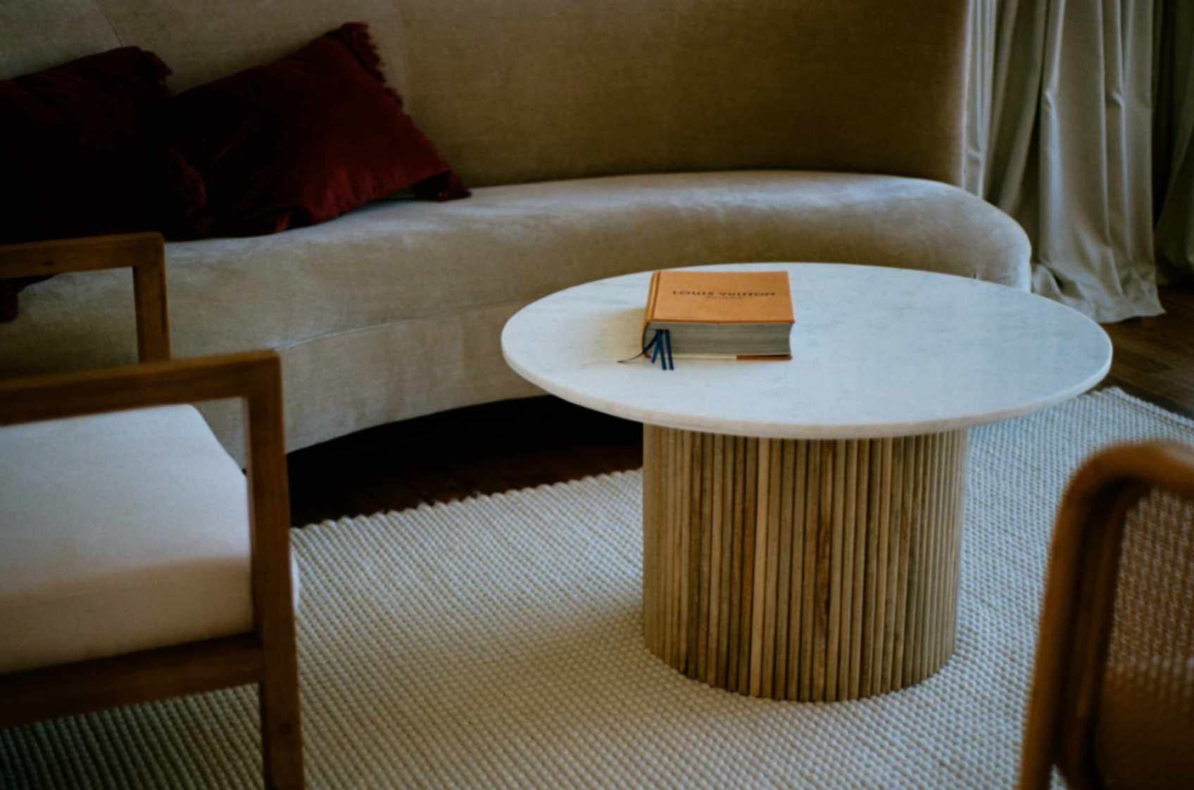 Living room inside this Merimbula accommodation with couches, pillows, chairs, and circular table in middle with book on top